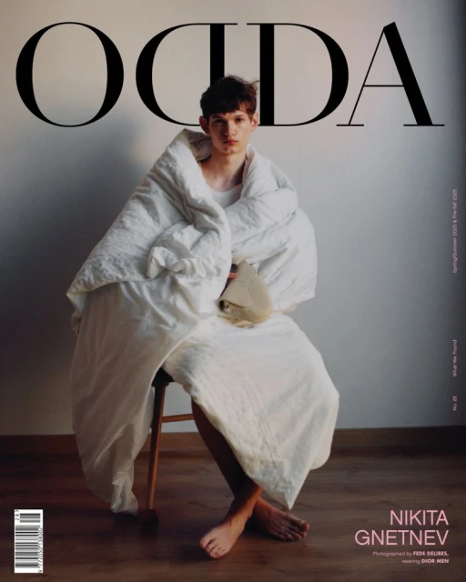 Magazine cover featuring a young man seated on a wooden stool, wrapped in a white blanket with large text 'OCDA' at the top.