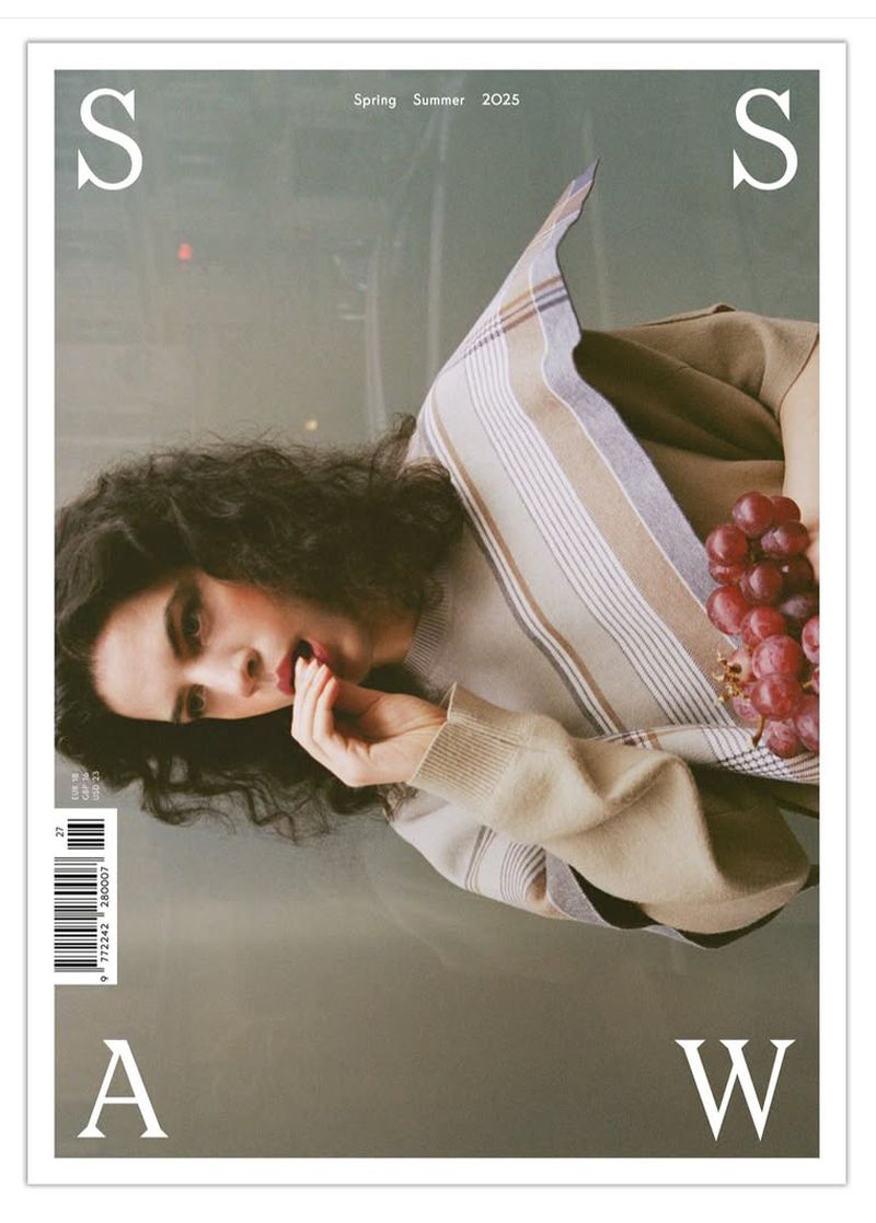 Magazine cover featuring a brunette woman holding a bunch of red grapes with beige and gray tones and large white typography elements.