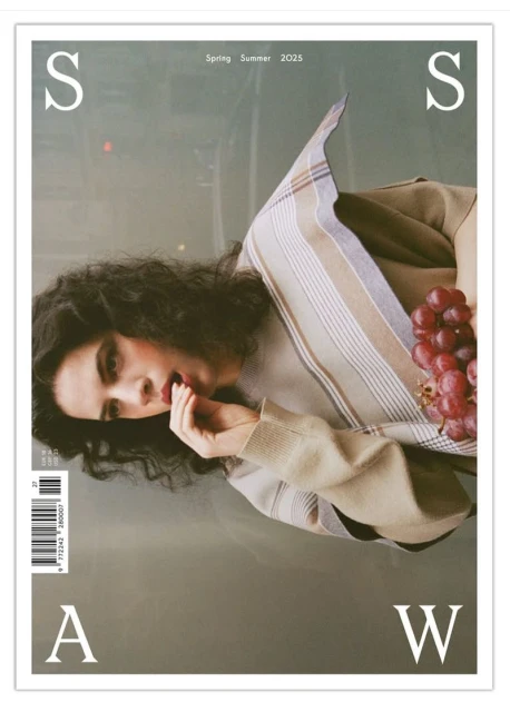 Magazine cover featuring a brunette woman holding a bunch of red grapes with beige and gray tones and large white typography elements.