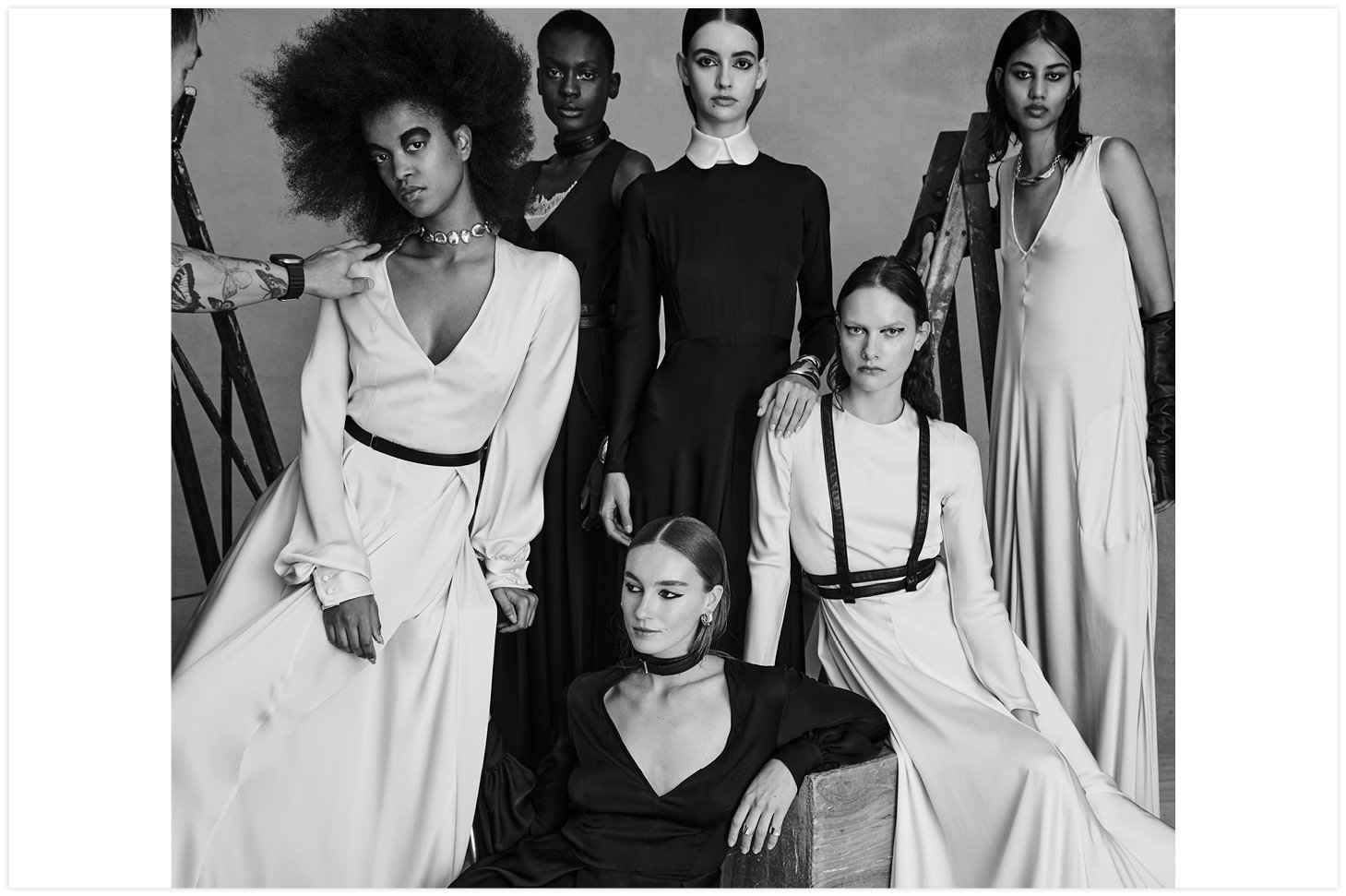 Group of diverse fashion models in dresses posing in a photo studio with neutral backdrop, captured in black and white.