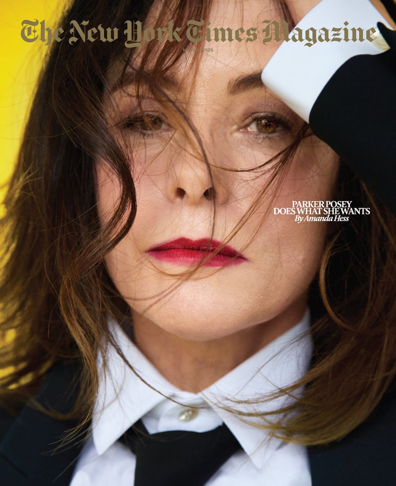 Close-up magazine cover portrait of adult woman with dark brown hair, red lipstick, and white shirt, posing in front of yellow backdrop.
