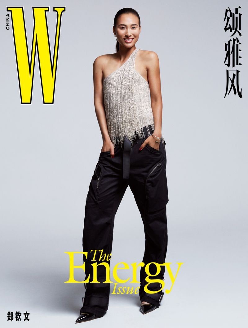 Magazine cover featuring a model in a one-shoulder top and black pants against a grey backdrop, text overlay. Fashion editorial shot.