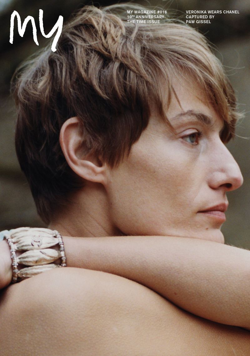 Close-up profile portrait of a short-haired woman resting her chin on her crossed arms, wearing a shell-beaded bracelet.