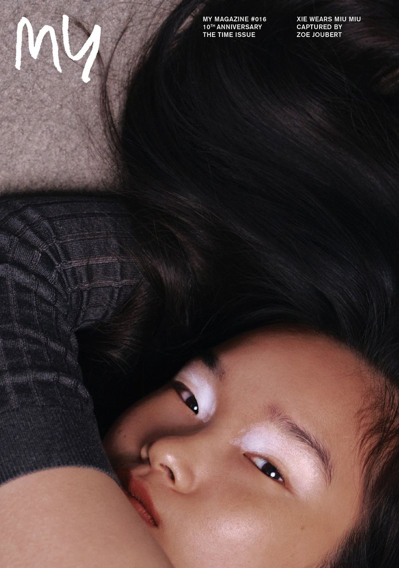 Close-up portrait of a model with dark flowing hair wearing a dark textured top against a neutral background for My Magazine.