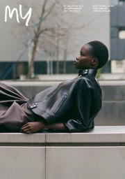Black model wearing a black leather jacket reclining against an outdoor concrete ledge for My Magazine.