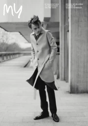 Monochrome fashion portrait of a young man wearing a light belted coat standing on a paved outdoor walkway