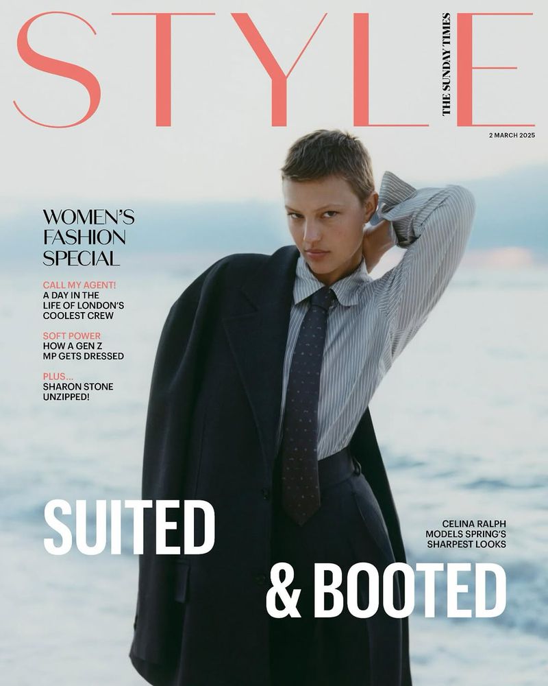 Magazine cover featuring a model in a suit and tie with a coat draped over her shoulder against a blurred outdoor background.