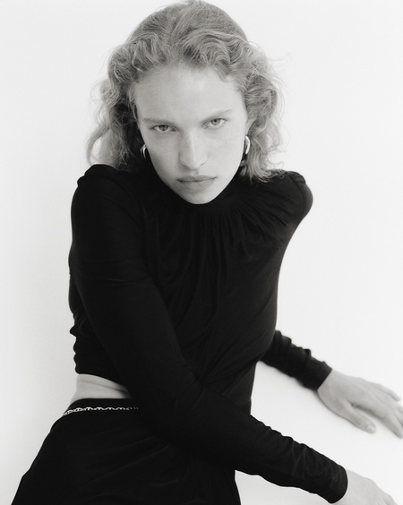 Monochrome portrait of a woman with curly hair wearing a long-sleeved black top against a white background in a studio setting.
