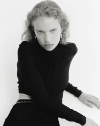 Portrait of a woman with curly hair wearing a black long-sleeve top against a white background