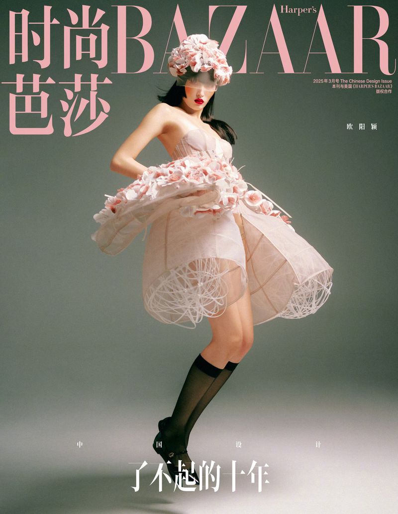 Magazine cover featuring a young woman in a pink dress with floral accents, set against a muted gray background. Fashion editorial.