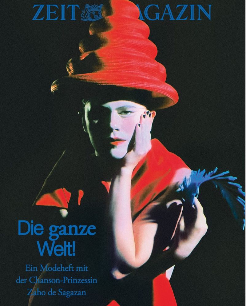 Magazine cover featuring a person with pale skin, wearing a red conical hat and red top, holding a blue bird-shaped object.