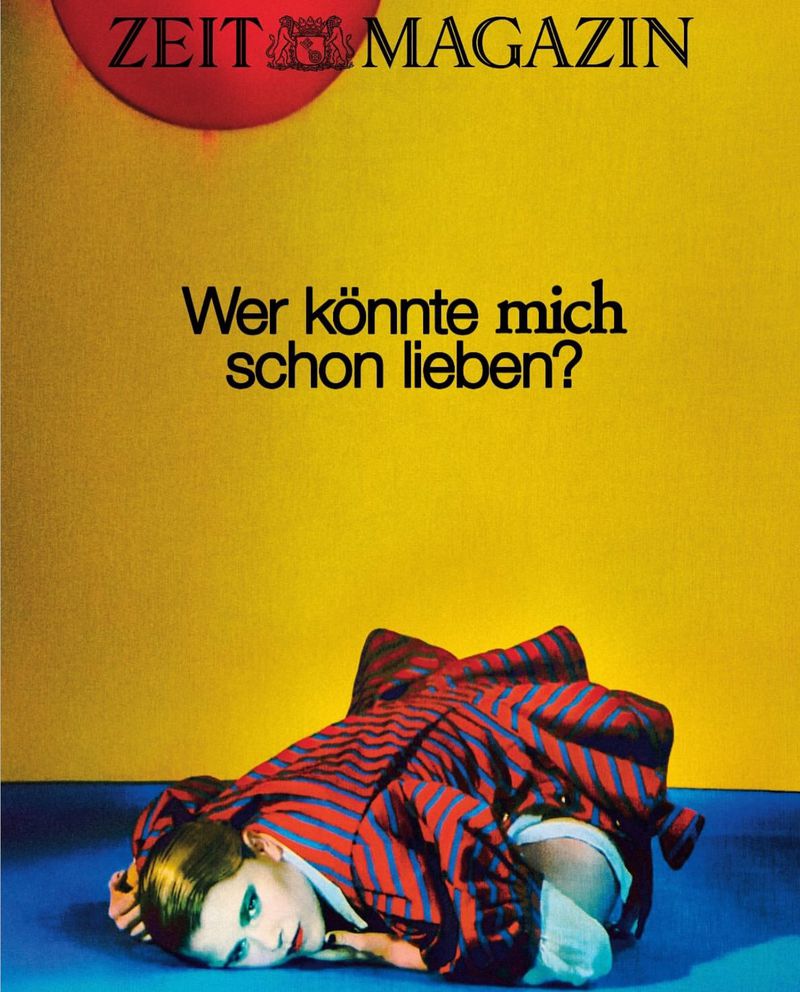 Magazine cover featuring a woman in a red and blue striped coat lying on a blue floor against a yellow wall with German text.