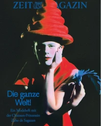 Zaho de Sagazan wearing a tall tiered red hat and red dress against a dark background for Zeit Magazine