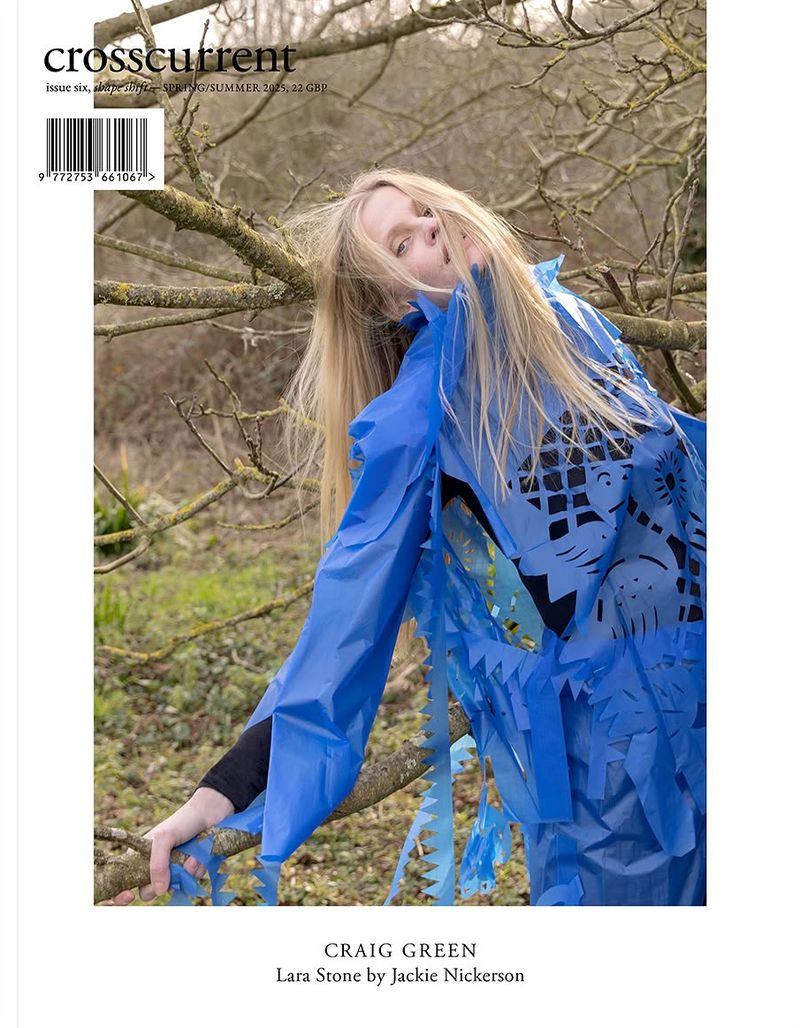 Crosscurrent magazine cover featuring a woman in a blue paper outfit, photographed outdoors with trees visible in the background.