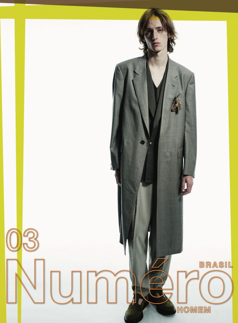 Magazine cover featuring a tall, slender man in a grey coat and khaki pants, posing against a bright white background with yellow accents.