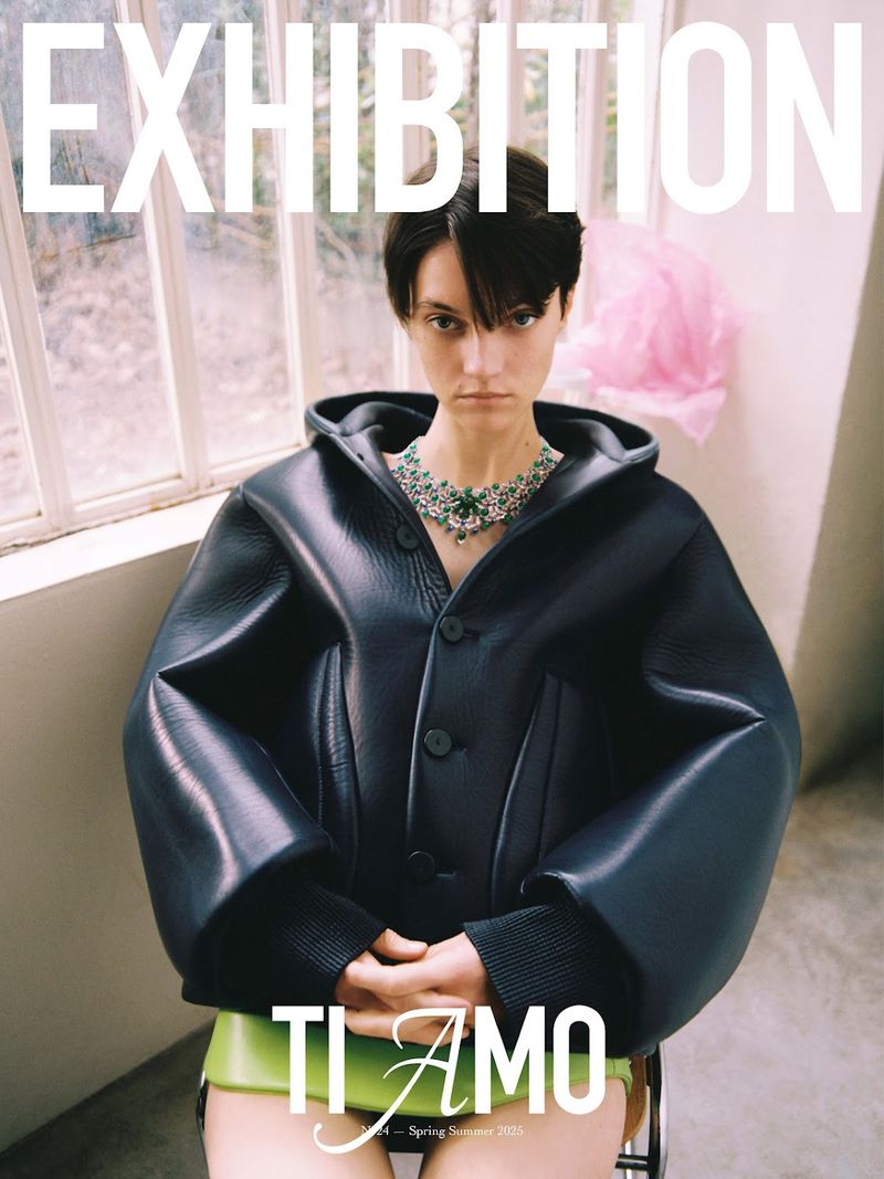 Fashion magazine cover featuring a woman wearing a black jacket and green jewel necklace indoors with an exhibition headline and text.