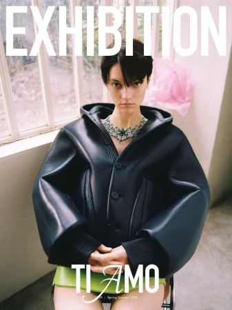 Fashion magazine cover featuring a woman wearing a black jacket and green jewel necklace indoors with an exhibition headline and text.