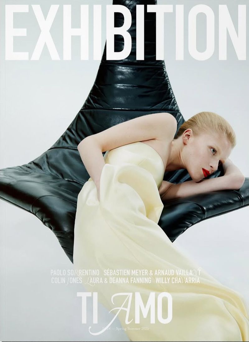 Fashion editorial featuring a fair-skinned woman in an off-white gown, leaning against a black leather chair against a clean white backdrop.