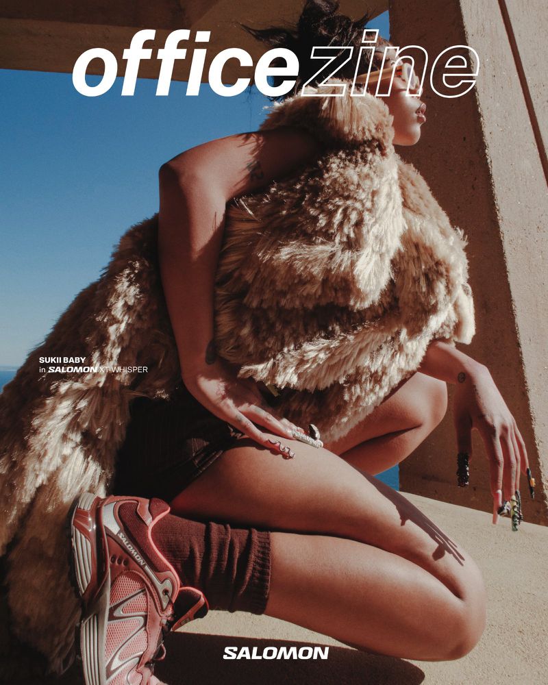 Magazine cover shot outdoors with a woman in a fur coat and athletic shoes kneeling in bright sunlight in front of a blue sky.