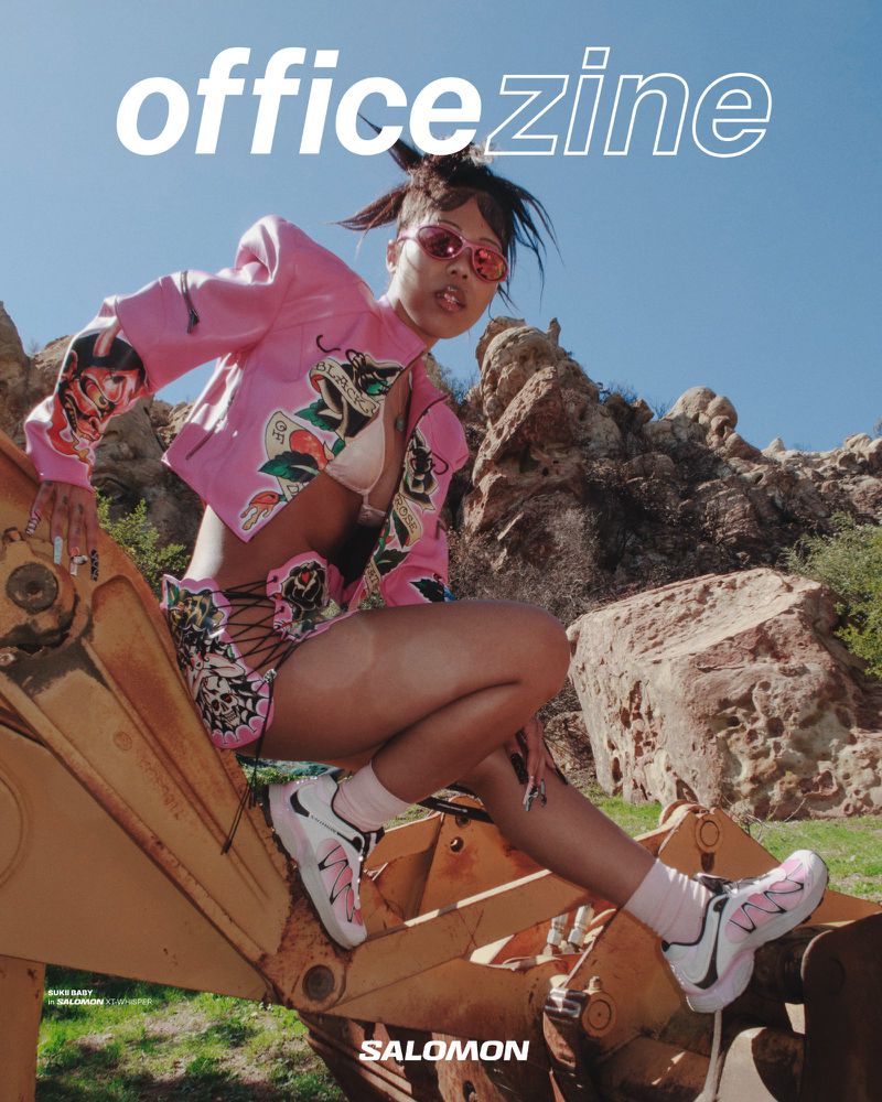 Magazine cover featuring a woman in pink jacket and shorts posing on construction equipment against a rocky, blue sky background.
