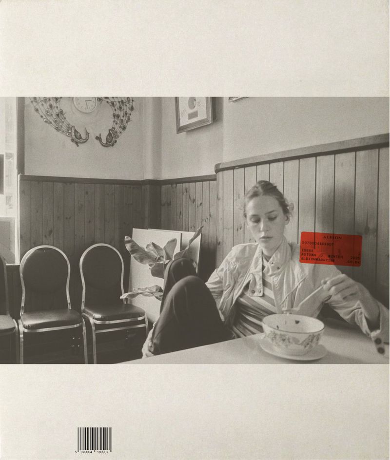 A woman seated at a wooden diner table holding chopsticks with a bowl of food, set against wood-paneled walls.