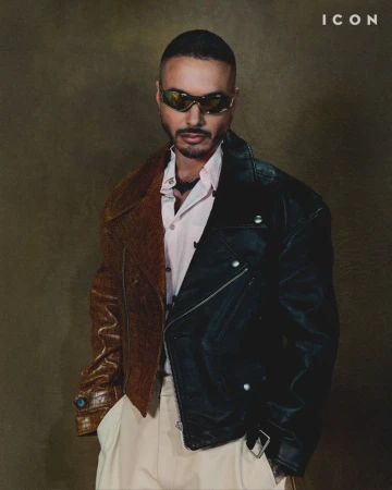 Portrait of J Balvin wearing sunglasses and a two-tone leather jacket against a muted brown background with 'ICON' text in the upper corner.