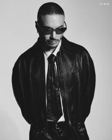 J Balvin in a black leather jacket and tie wearing sunglasses against a light background for ICON Magazine Mena