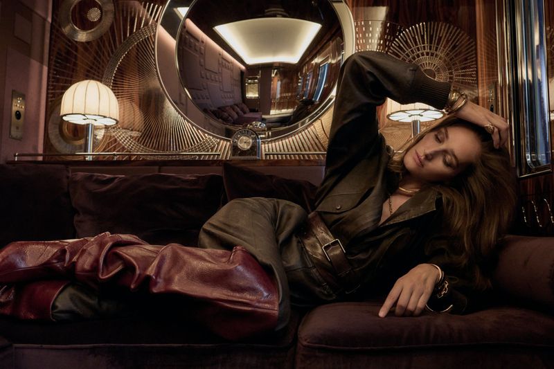 Model Josephine Le Tutour reclining on a luxury train sofa in a brown leather outfit for Madame Figaro.