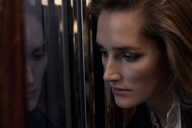 Close-up portrait of a woman looking out a train window with her reflection visible in the glass