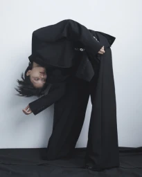 Model in a black suit bending backward against a seamless white background for Vogue Thailand shot by Paul Scala