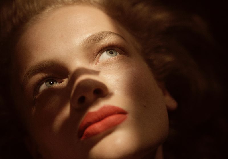 Close-up portrait of a woman with vibrant red lipstick and dramatic directional lighting across her face.
