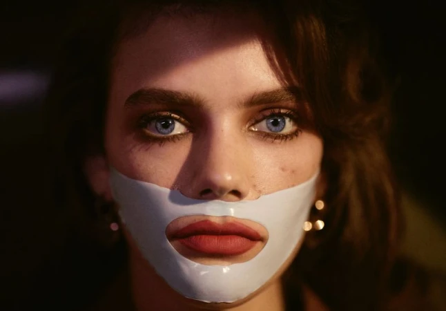 Close-up portrait of a woman with vibrant blue eyes wearing a white lower face mask and bold red lipstick