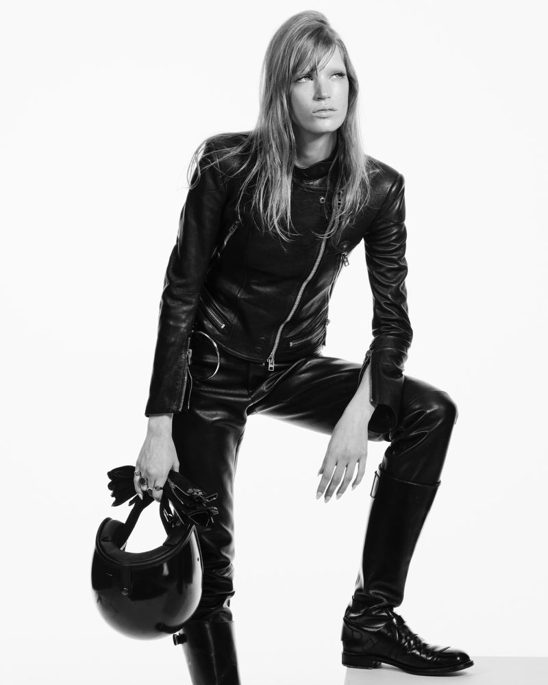 A woman in a black leather outfit poses with a motorcycle helmet against a bright background in a high-contrast fashion shot.