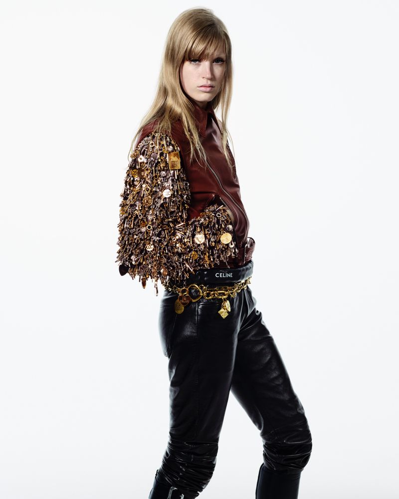 Fashion shot of a woman posing in a brown leather jacket with decorative sleeves and black leather pants against a white backdrop.
