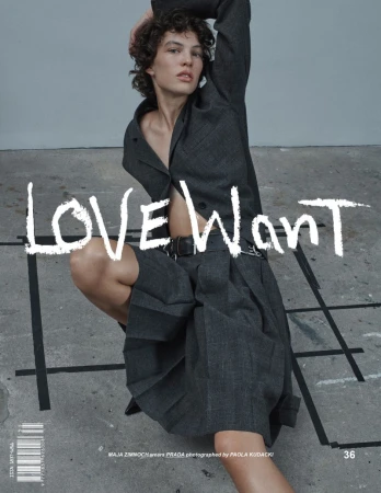 Woman in dark grey jacket and skirt crouching indoors. Magazine cover, LoveWant printed. Fashion editorial shot with natural light.