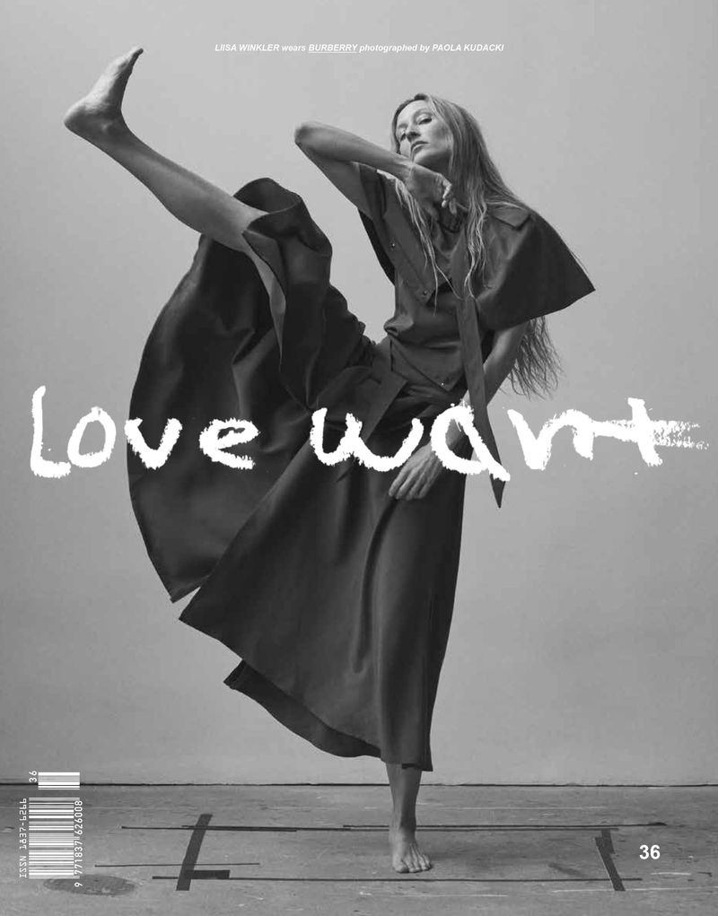 Black and white fashion shot of a slender adult female model in a draped dress and bare feet striking a dynamic pose on a grey surface.