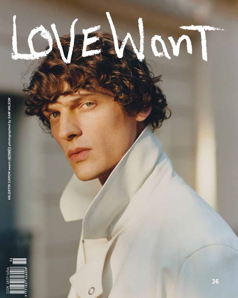 Close-up portrait of a male model with curly brown hair wearing a white high-collar jacket for Love Want Magazine