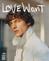 Close-up portrait of a male model with curly brown hair wearing a white high-collar jacket for Love Want Magazine