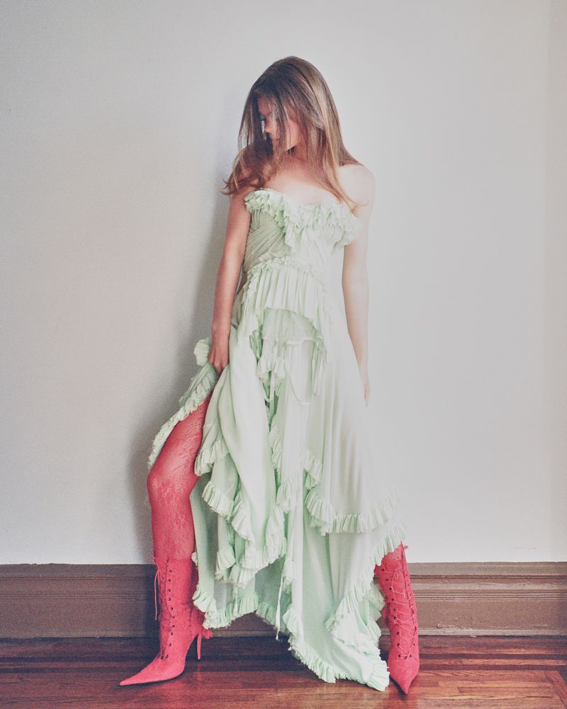 Model in pale green ruffled dress and pink boots standing against a neutral wall for Harper's Bazaar Thailand project Pillow Talk.