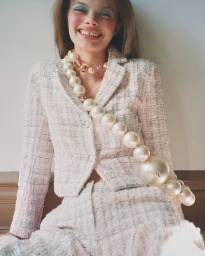 Smiling model wearing a light pink tweed jacket and skirt with an oversized pearl crossbody necklace for Harper's Bazaar Thailand