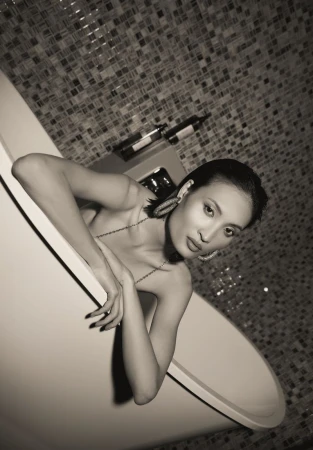 Woman in bathtub with wine bottle, moody monochrome portrait. Bathroom with patterned tile. Dark, intimate beauty shot. 