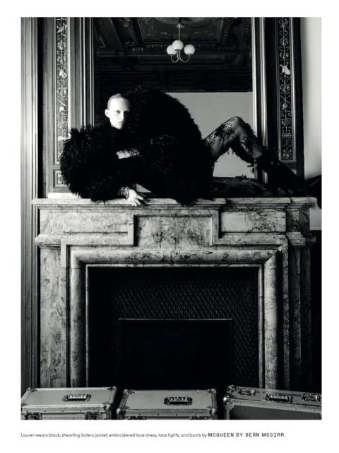 Fashion shot of a person in a black, shaggy bolero jacket and lace tights lying on a marble fireplace mantelpiece with aluminum cases.