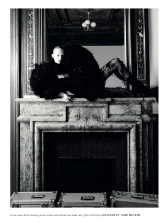 Fashion shot of a person in a black, shaggy bolero jacket and lace tights lying on a marble fireplace mantelpiece with aluminum cases.