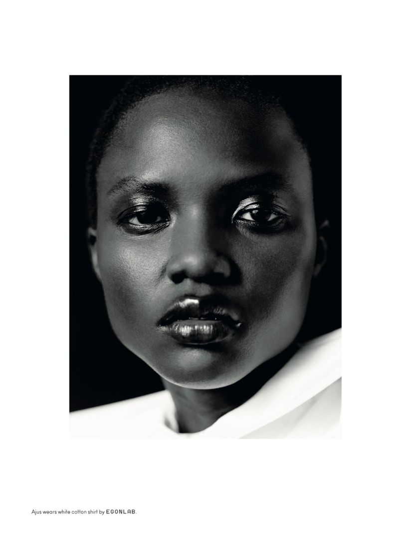 Striking black-and-white close-up of a woman with dark skin wearing a white collared shirt against a dark backdrop, fashion editorial.