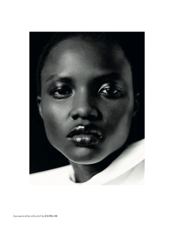 Striking black-and-white close-up of a woman with dark skin wearing a white collared shirt against a dark backdrop, fashion editorial.