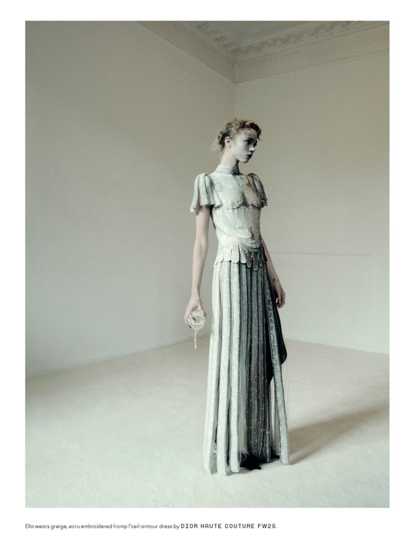 Fashion shot of a female model wearing a long, formal dress with lace details in a minimalist photo studio with high ceilings.