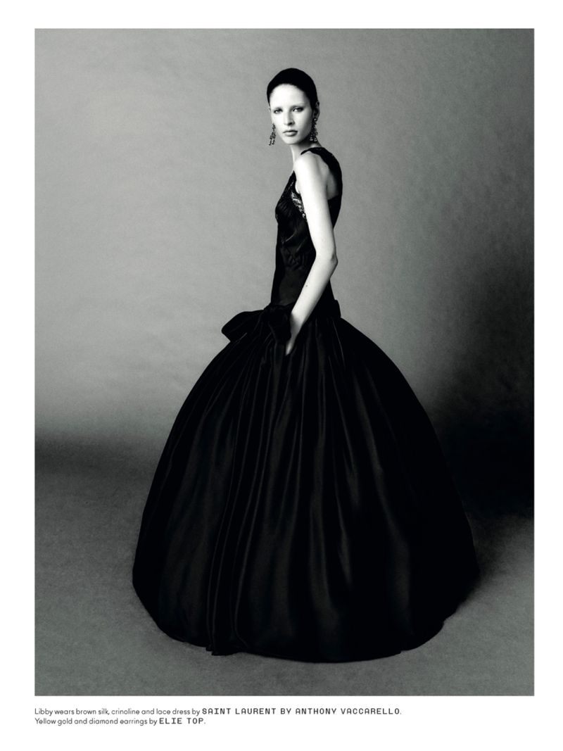 Elegant fashion portrait of a woman in a black silk gown with gold and diamond earrings, against a gray backdrop in a photo studio.