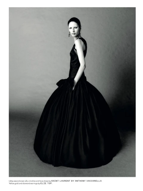 Elegant fashion portrait of a woman in a black silk gown with gold and diamond earrings, against a gray backdrop in a photo studio.