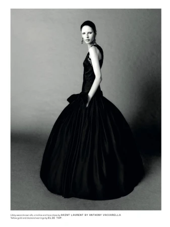 Elegant fashion portrait of a woman in a black silk gown with gold and diamond earrings, against a gray backdrop in a photo studio.