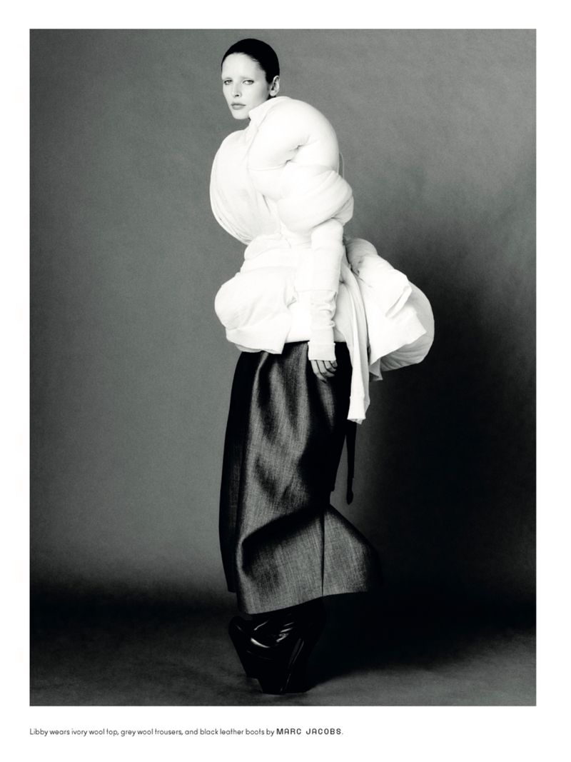 Editorial fashion shot: Woman in avant-garde white top, grey wool trousers, and black leather boots in a studio setting.